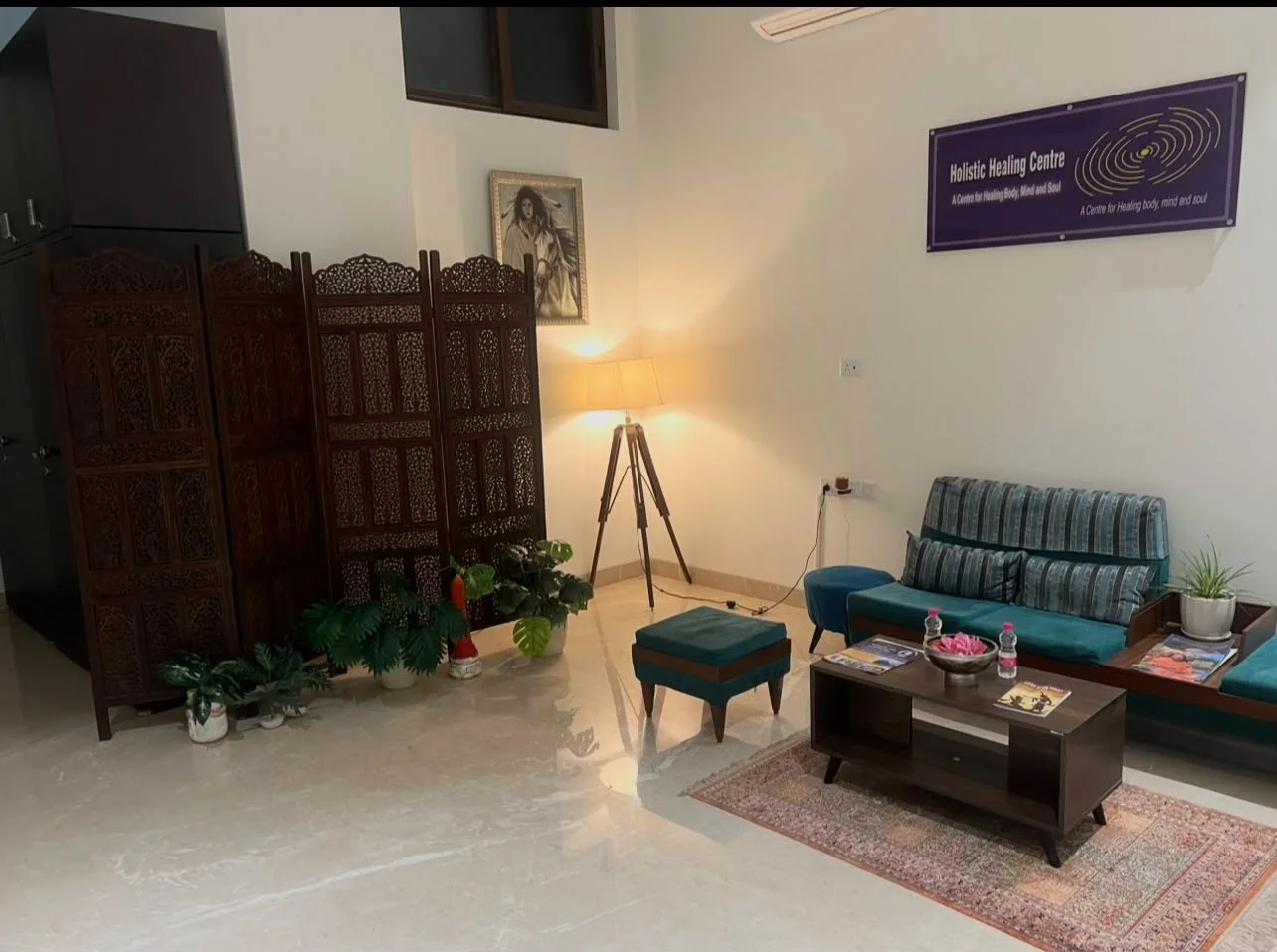 The lounge at Holistic Healing Centre, with a carved wooden screen, a lamp, a teal sofa and the centre’s sign